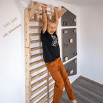 Kind an der Klimmzugstange des LOOPO JUNGLE neben einer Kletterwand